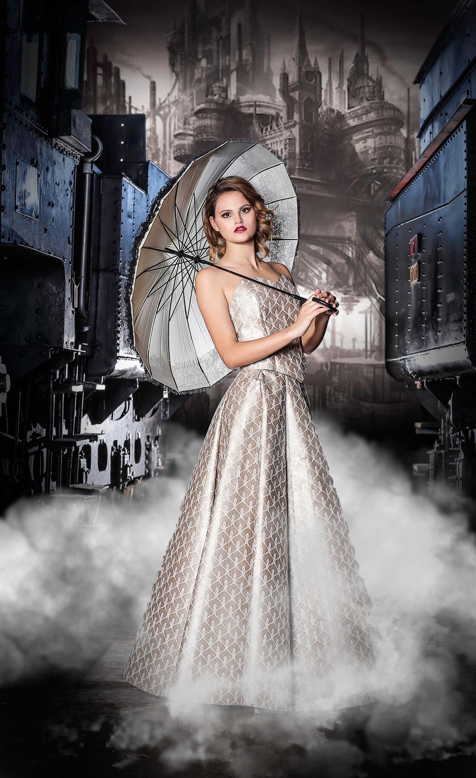 Luxury steampunk couture gown by Toni Hamler, crafted from wallpaper, showcased in an industrial fantasy setting with locomotives and misty cityscape.