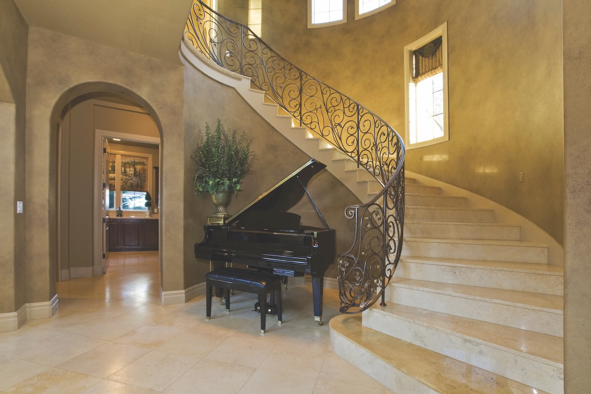 Elegant curved staircase with custom decorative finishes and a black grand piano, reflecting Toni Hamler’s luxury interior style.