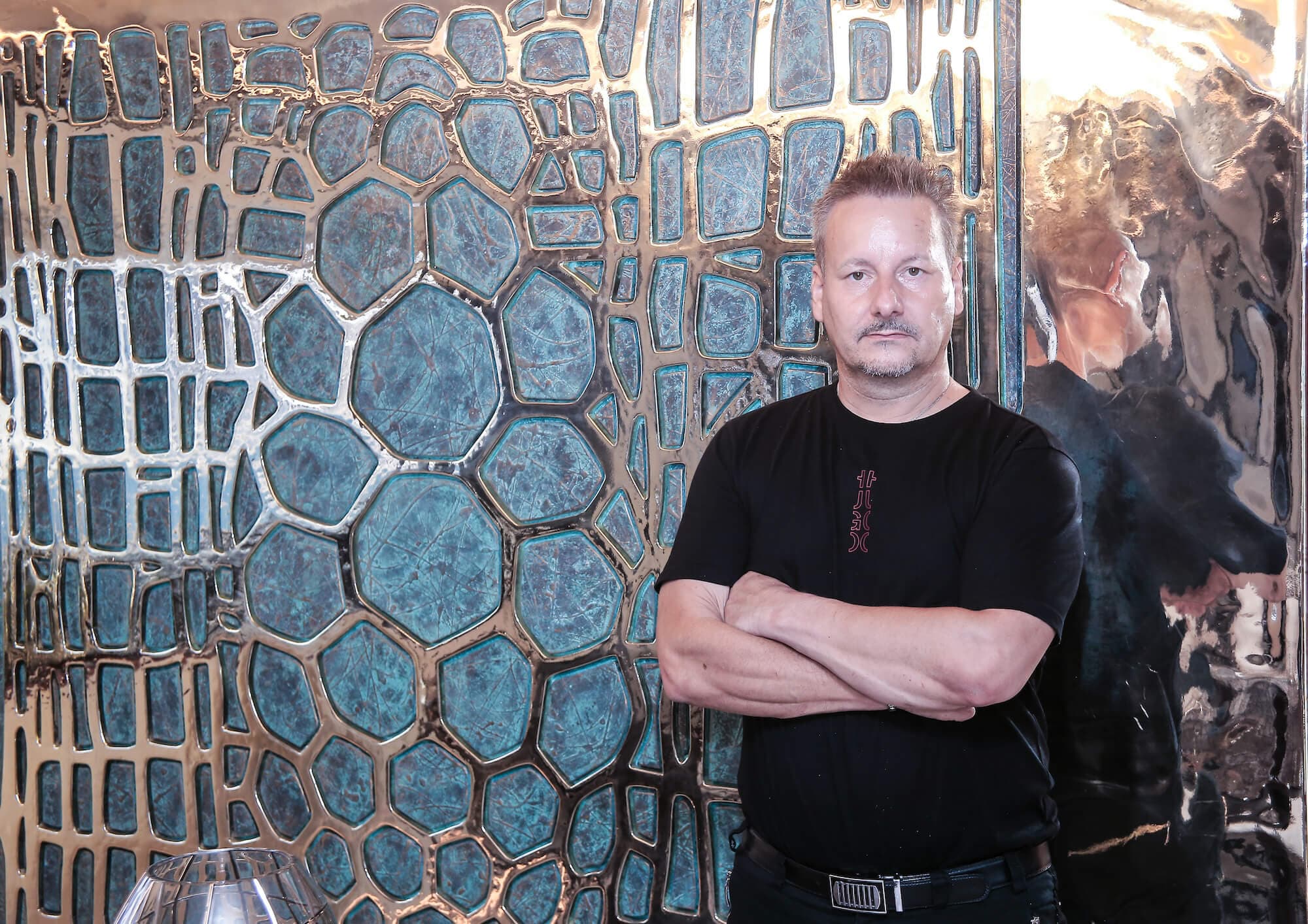 Toni Hamler in front of a luxury yacht interior featuring a bespoke metallic and textured wall installation, showcasing his expertise in high-end custom design and decorative arts.