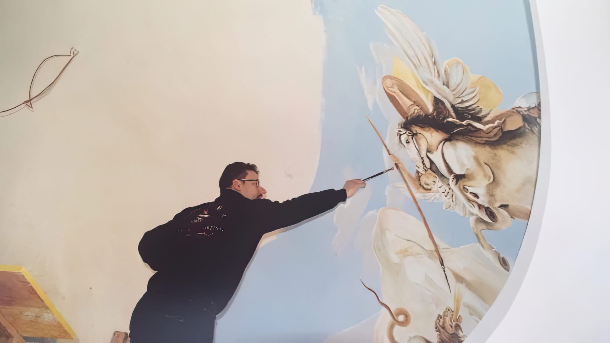 Toni Hamler painting a ceiling fresco with intricate historical details, showcasing his expertise in classical mural and ceiling artwork.