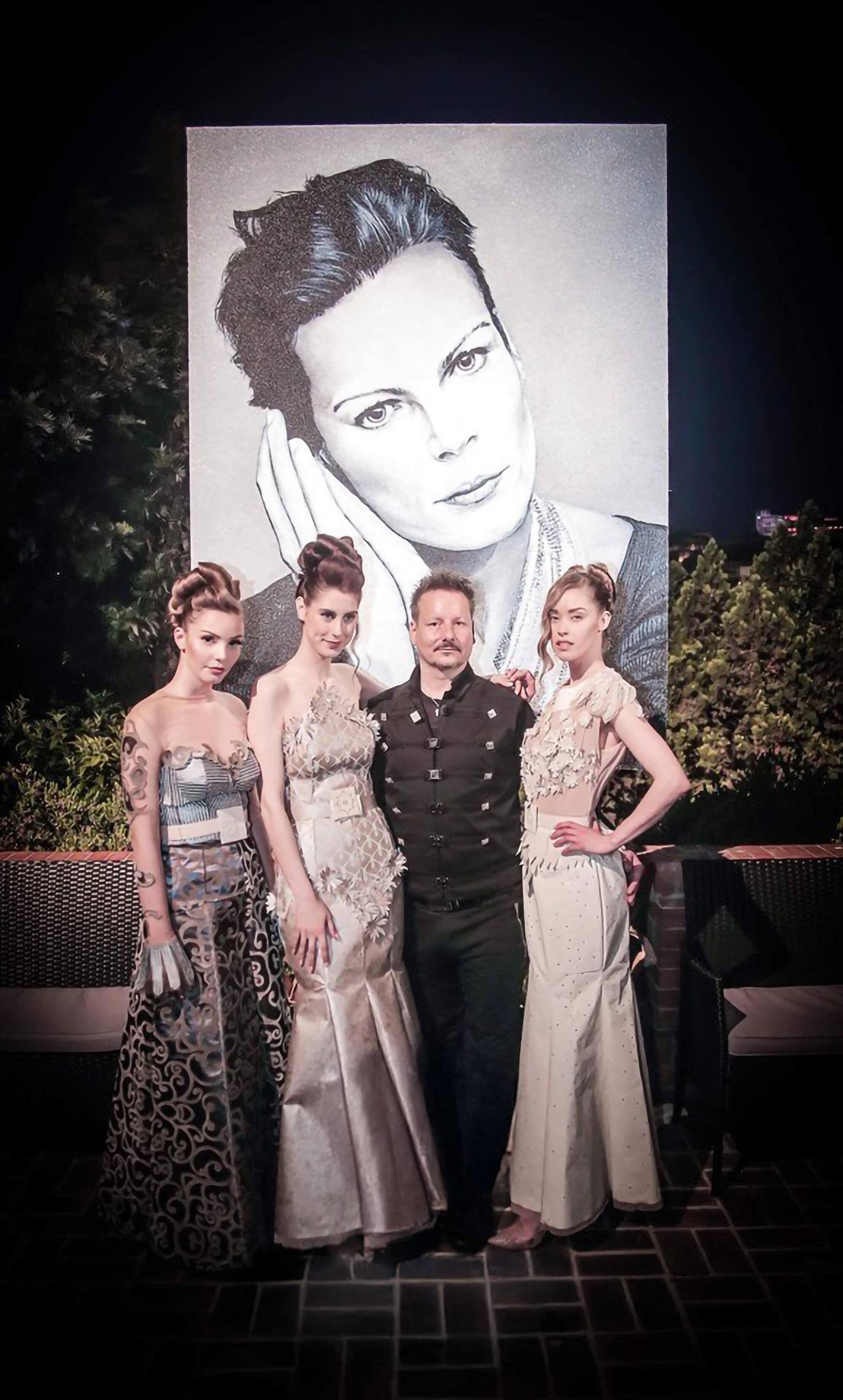 Toni Hamler with models wearing his bespoke wallpaper couture dresses, standing in front of a large-scale portrait of Princess of Monaco, showcasing a fusion of fashion and fine art.