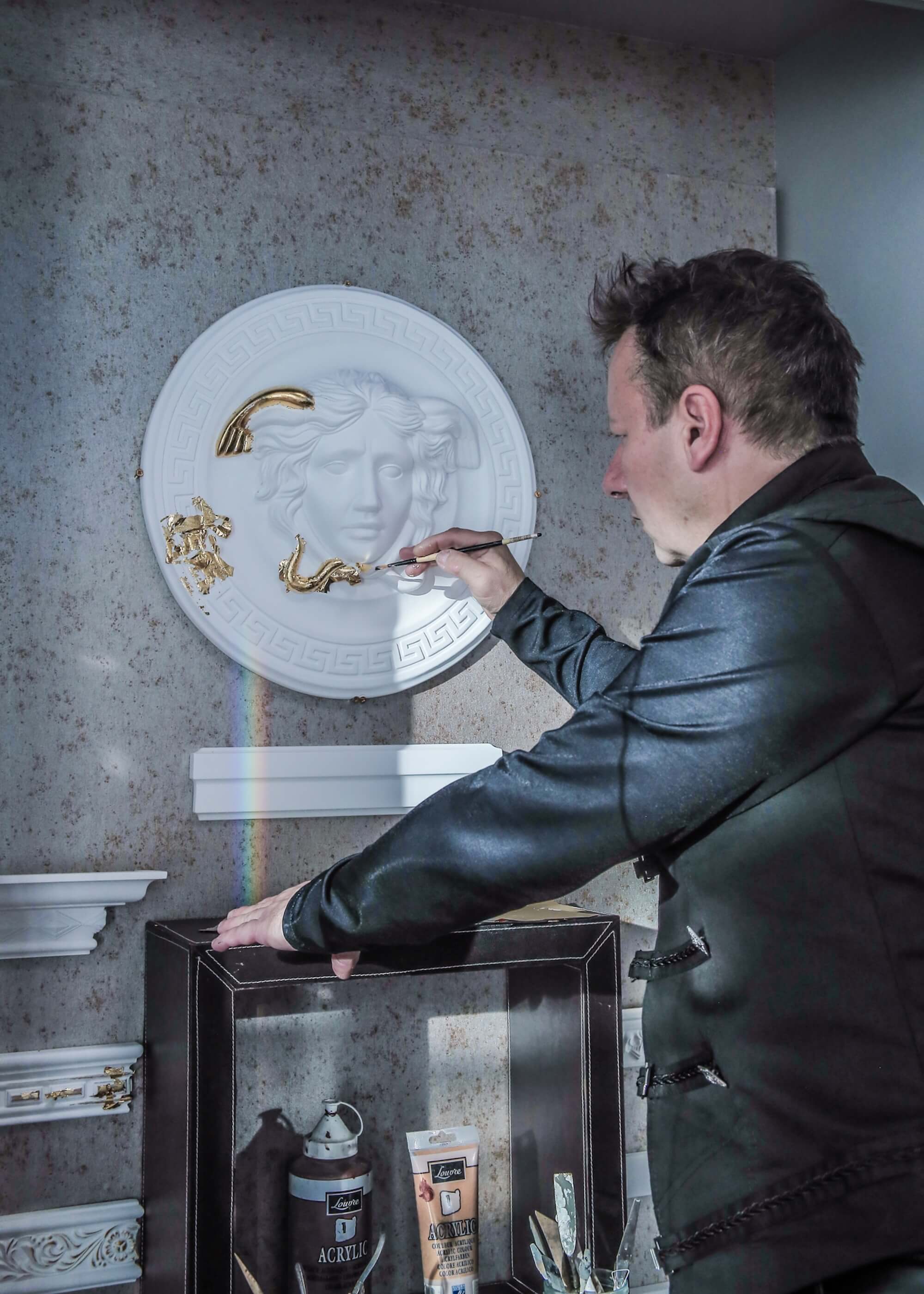 Toni Hamler hand-gilding a bespoke Medusa wall relief, showcasing precision craftsmanship and the fusion of classical art with luxury interior decor.