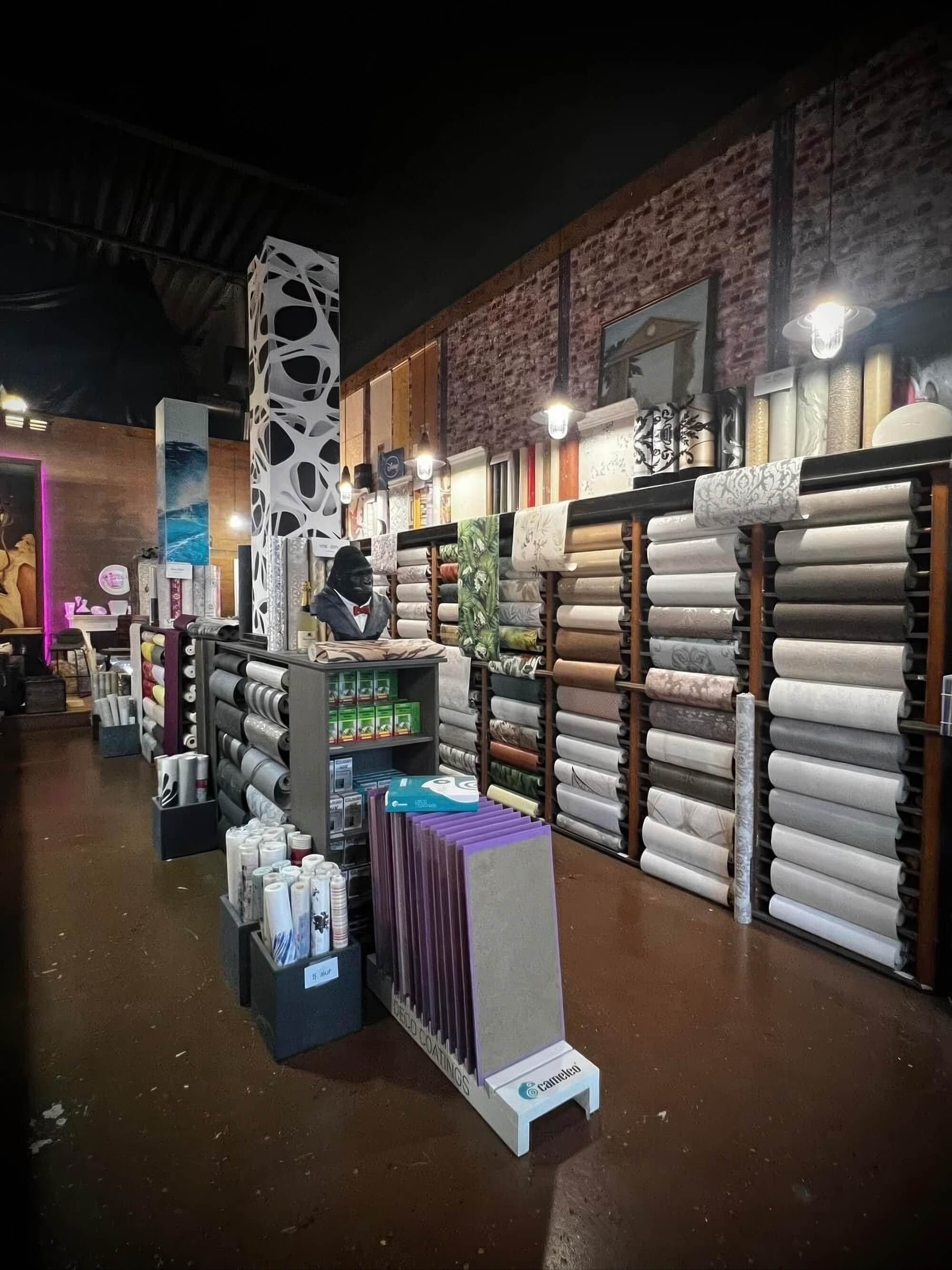 A spacious and well-lit wallpaper store interior with an extensive collection of wallpaper books and rolls.